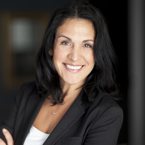 Business woman wearing black, leaning on the wall, and smiling